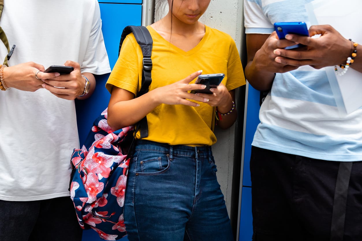 group of school students using cell phones against lockers