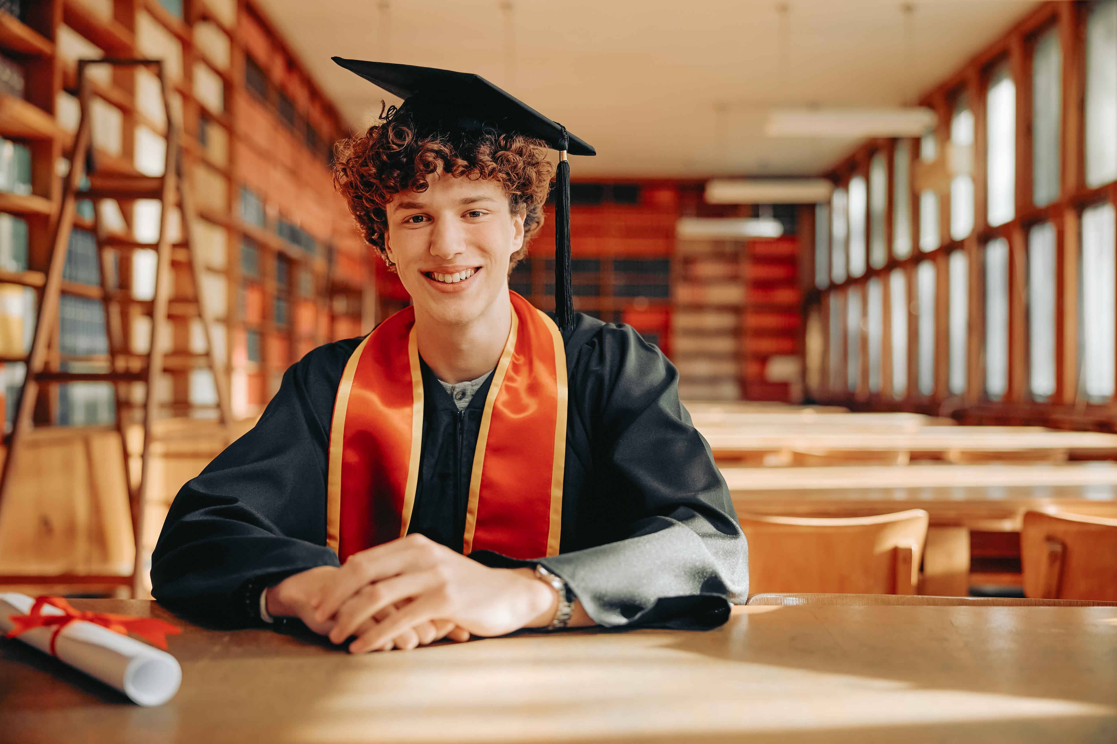 high school student sitting in cap and gown with diploma