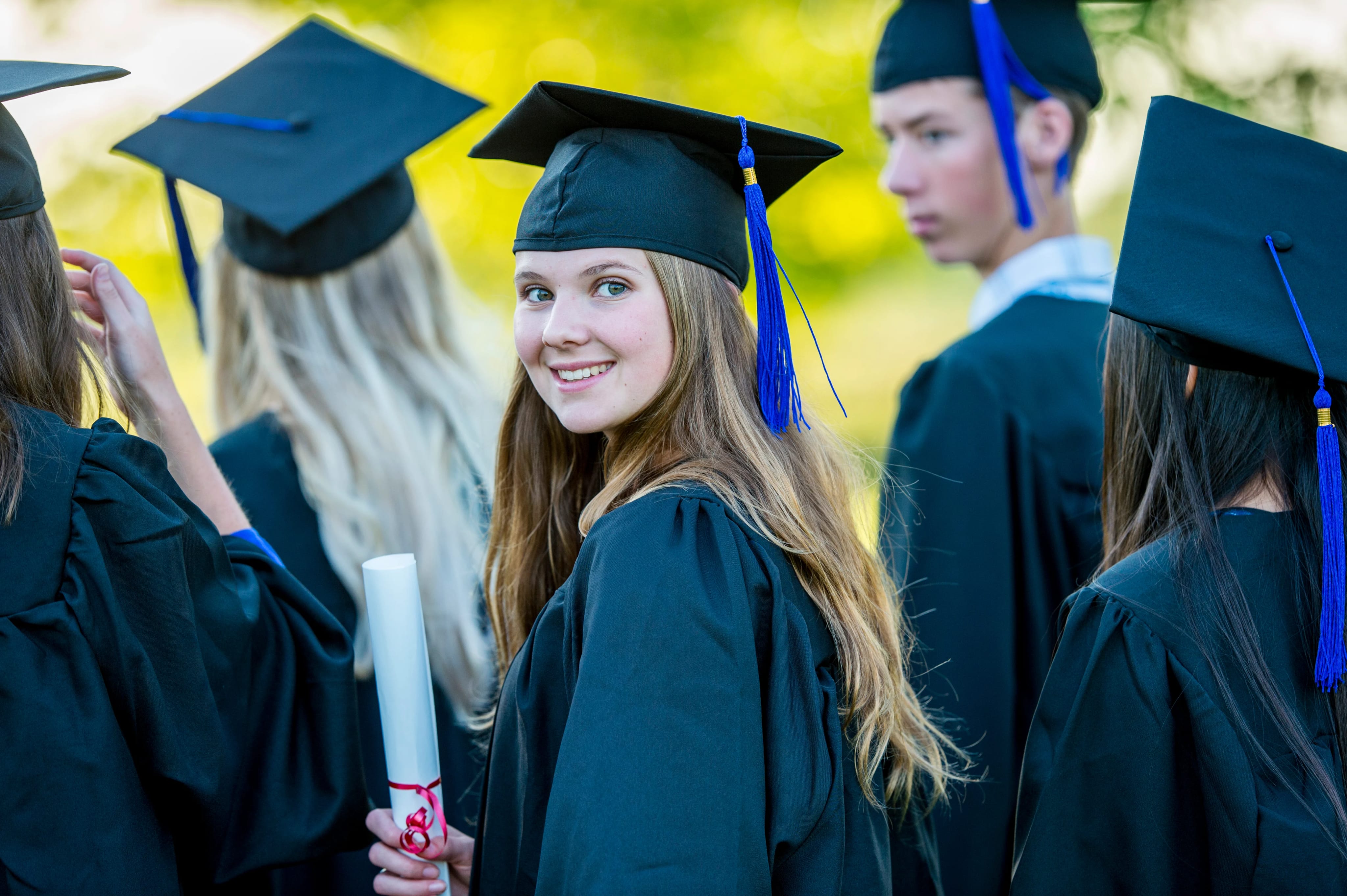 high school student holding diploma in cap and gown