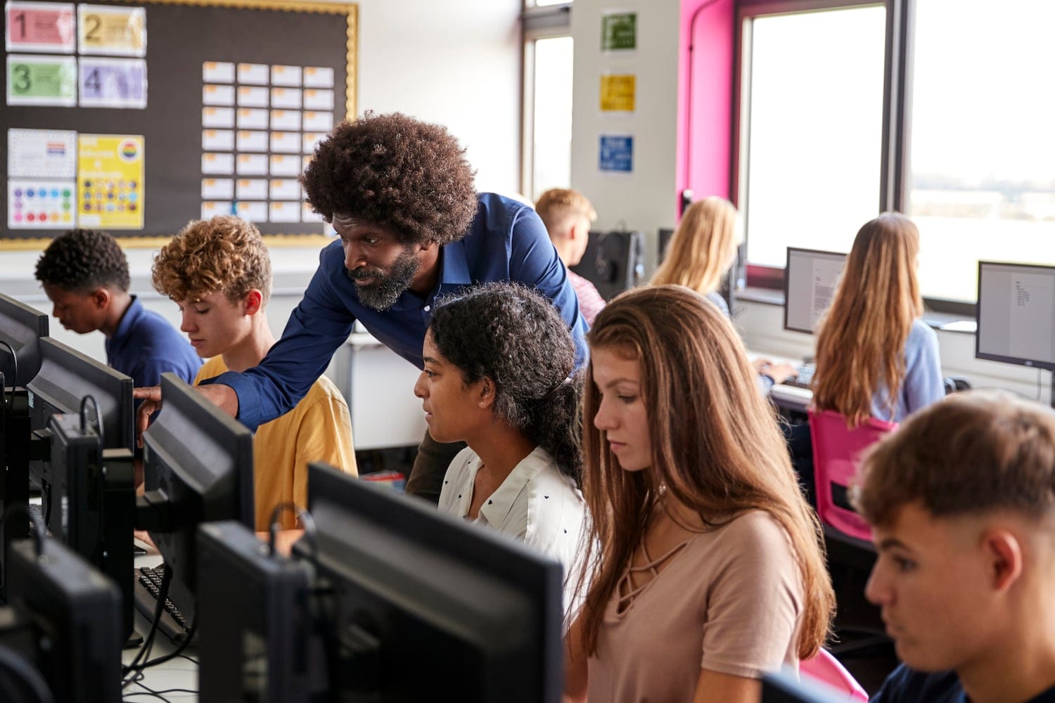 teacher working with high school students in a computer class